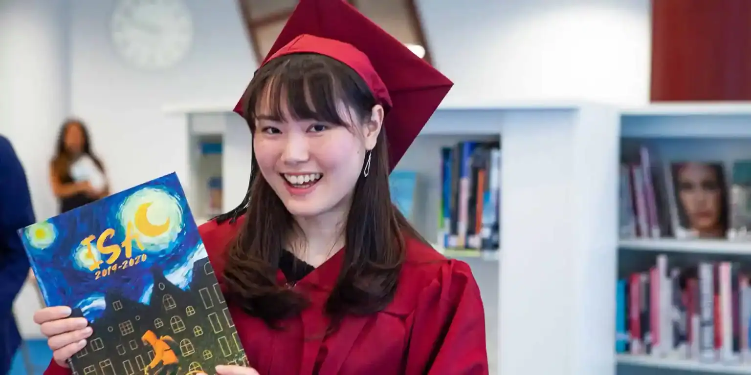 Młoda studentka w sukni dyplomowej trzymająca rocznik w nowoczesnej bibliotece.