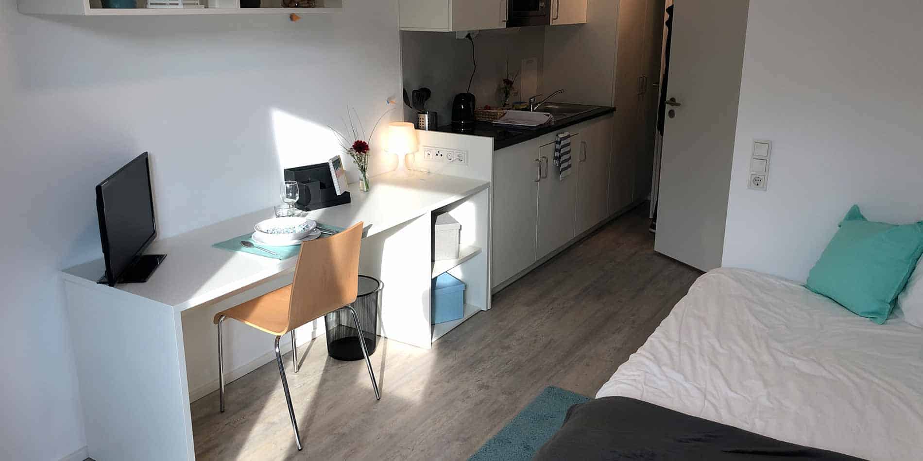 Apartamento compacto con espacio de trabajo, cocina americana y cama, ideal para alojamiento de estudiantes o vida moderna.