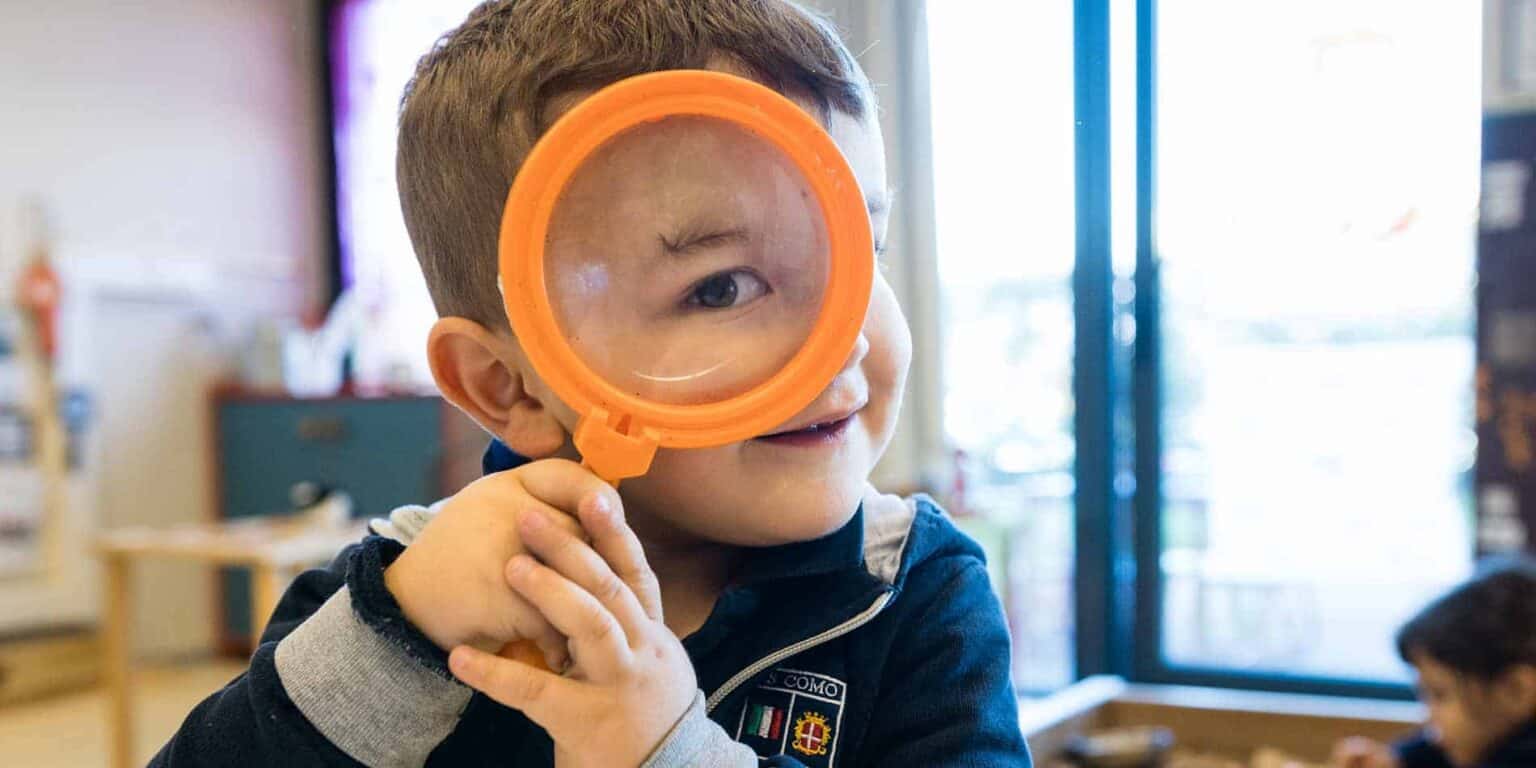 Bright young boy with magnifying glass, exploring learning at an international school.