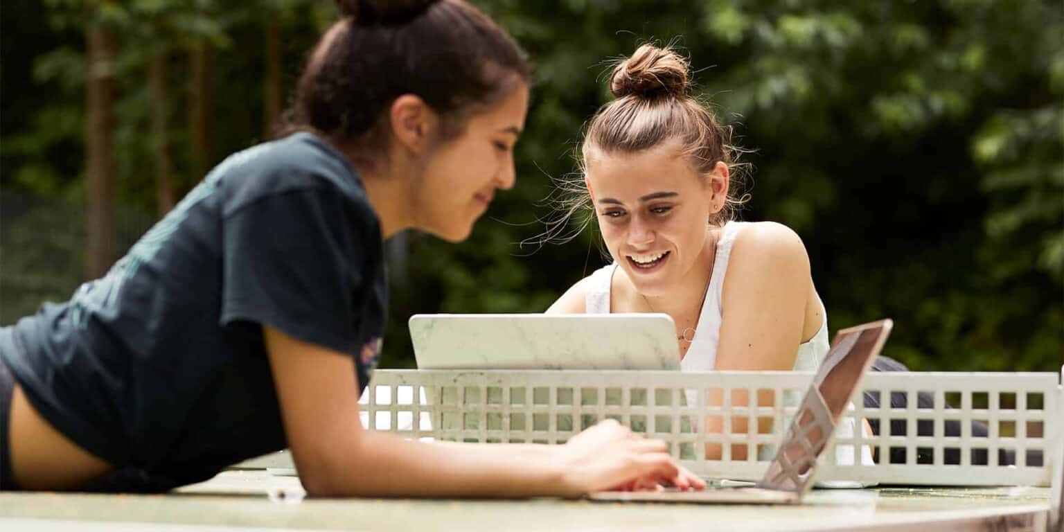 Bright smiling girls studying outdoors with laptop and tablet, young learners at international schools, educational success, student life.