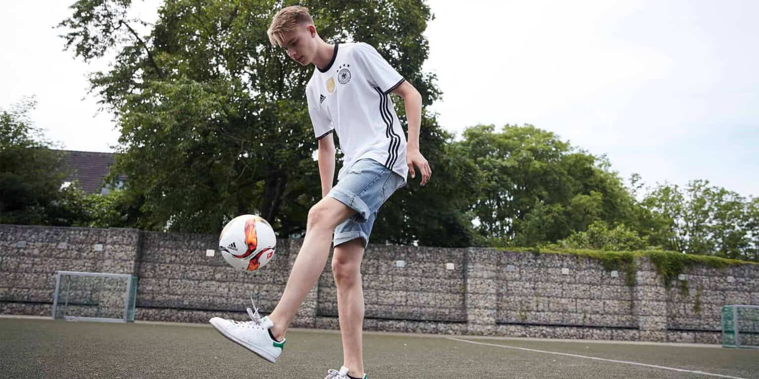 Youth football player practicing dribbling outdoors on school sports field.
