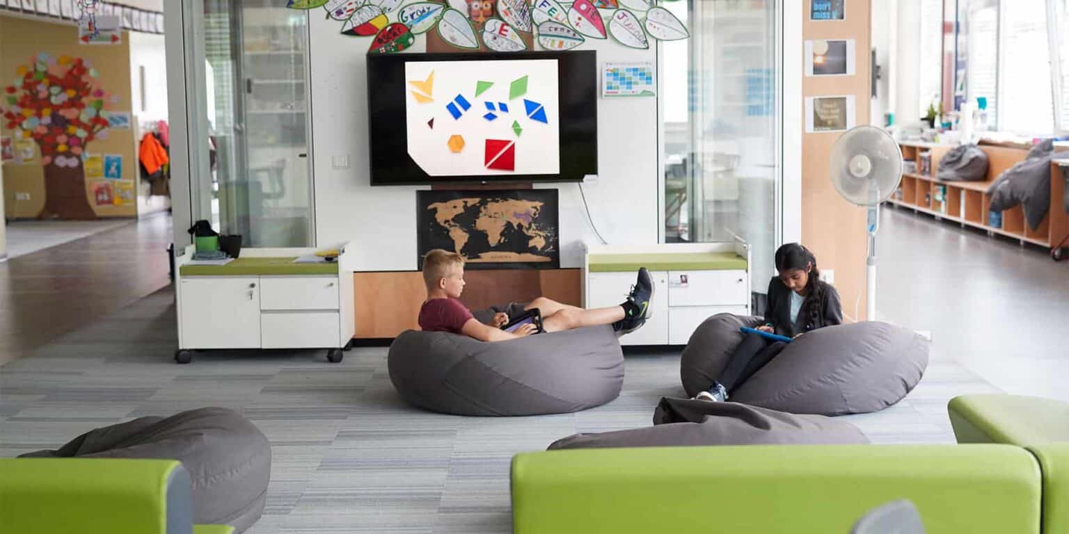 Relaxed students in a modern, colorful world school lounge with bean bags, interactive screens, and creative educational displays.