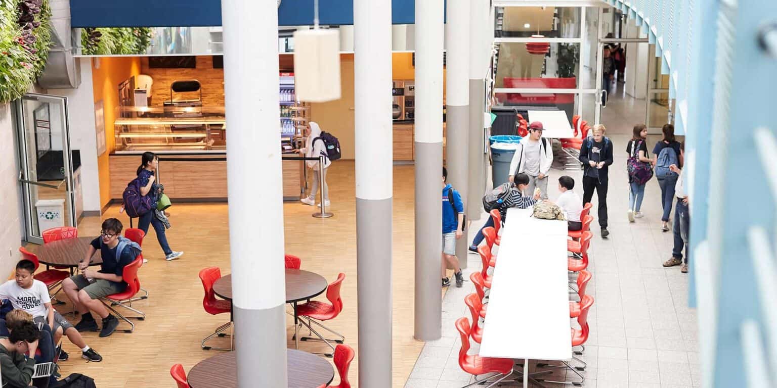 Students studying and socializing in a modern school cafeteria or common area.