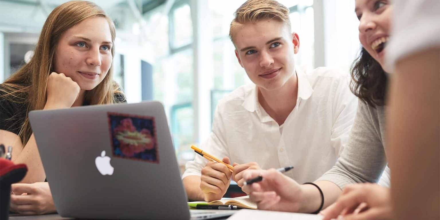 Young diverse students studying and collaborating at a school, using laptops and engaging in active learning.