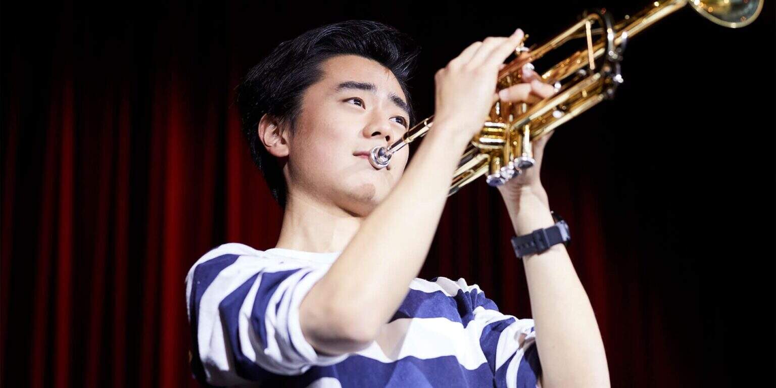 Young male student playing trumpet on stage at a school music event.