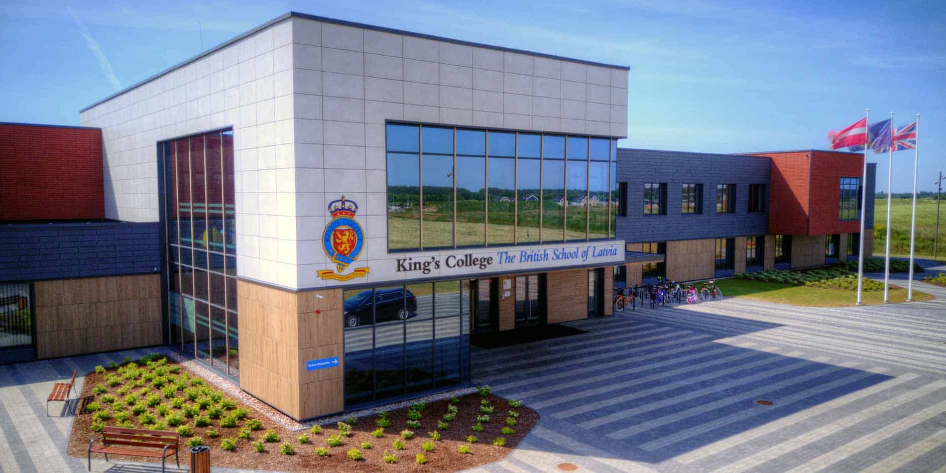 Школы 4 Modern British school building in Latvia with glass facade and flags, promoting international education.