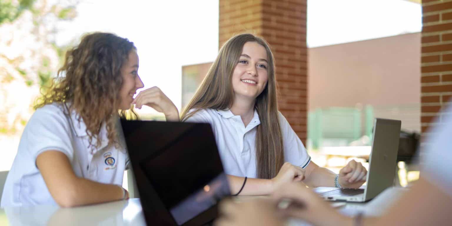 Students studying on laptops at a modern outdoor school campus.