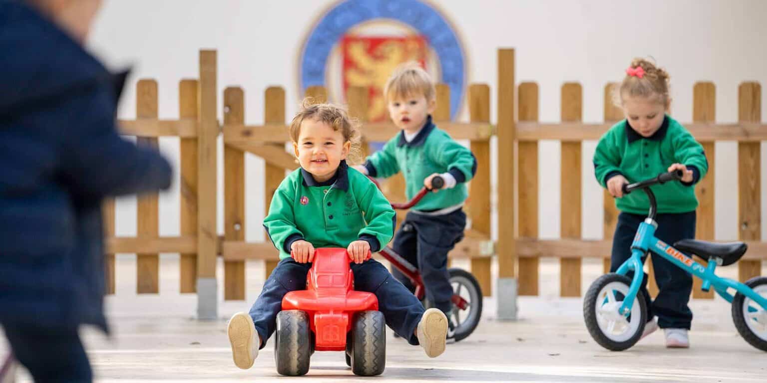 Young children playing outside at a world school, riding tricycles and bikes on a sunny day.