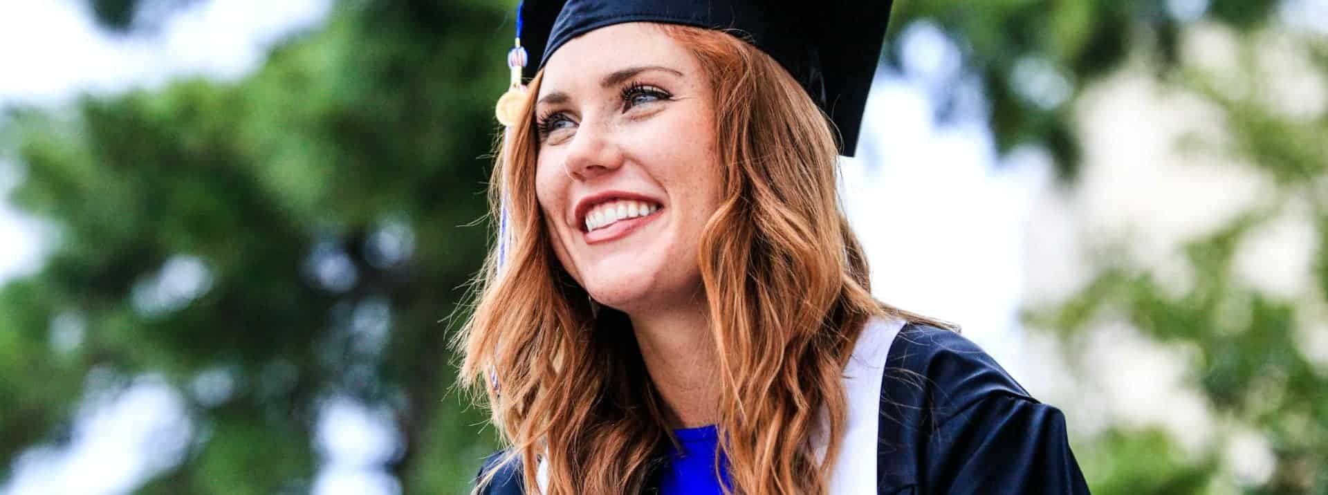 Bright young woman in graduation cap and gown celebrating academic achievement outdoors.