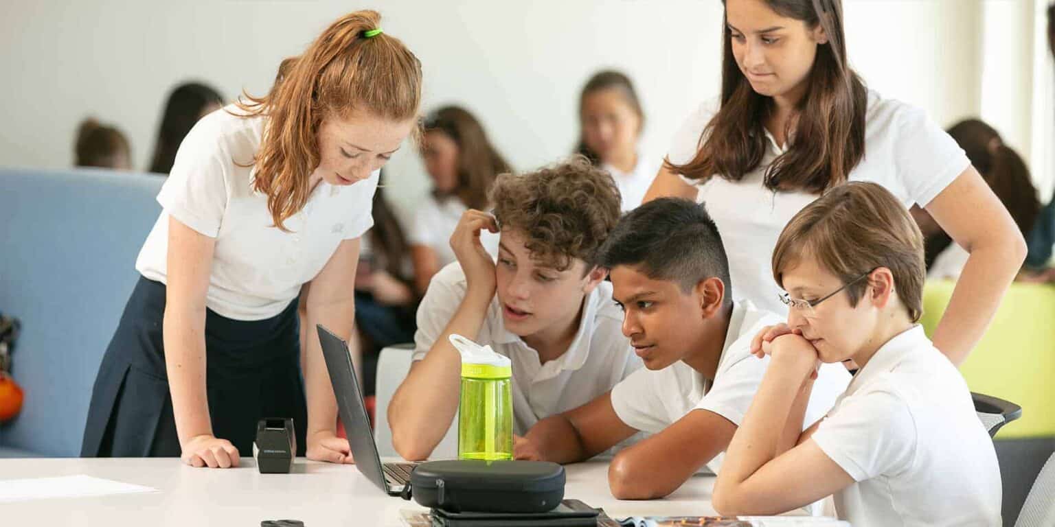 Curious students collaborating with teacher during a class project at a modern international school.