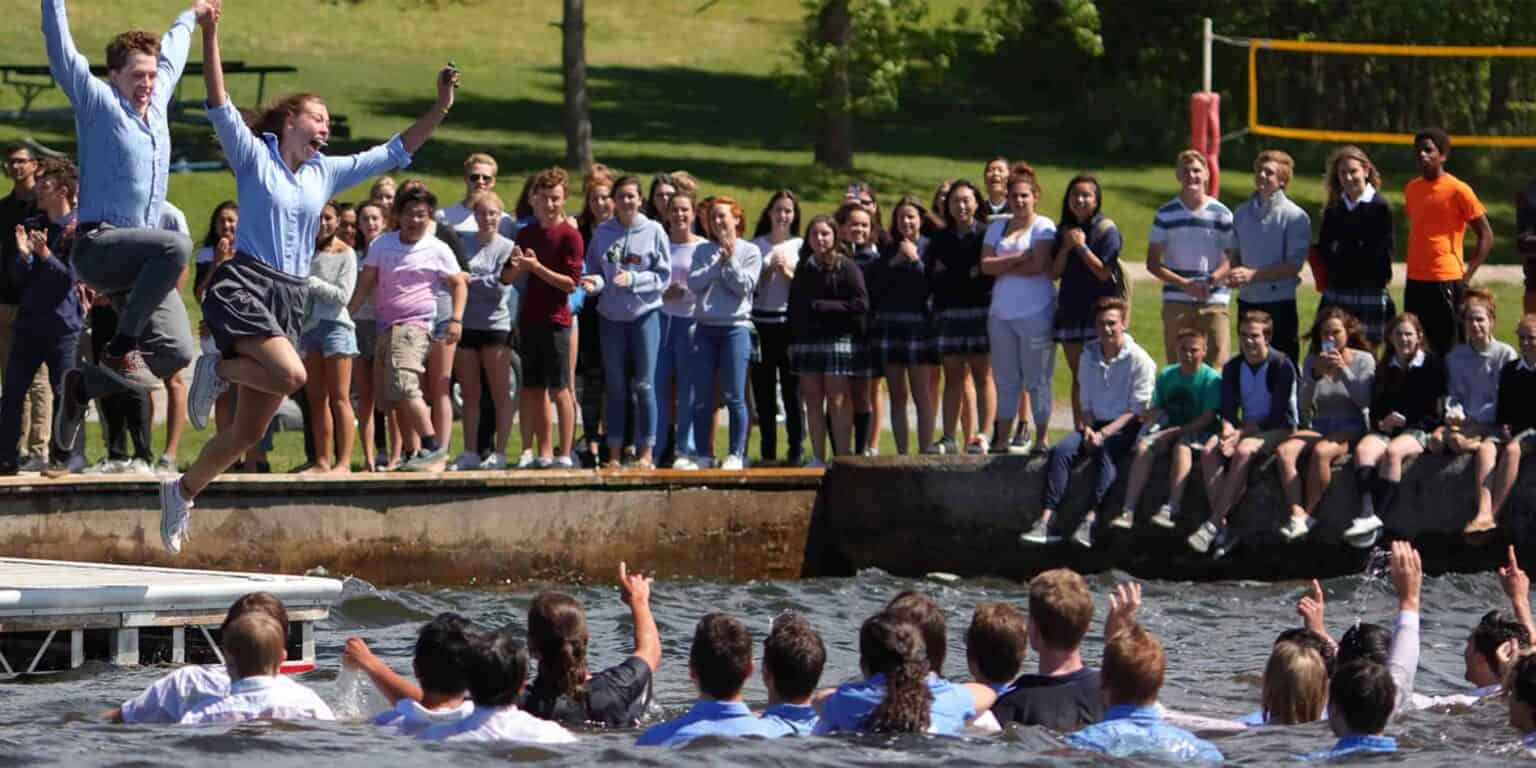 Jumping student during outdoor school activity with classmates watching by the water.
