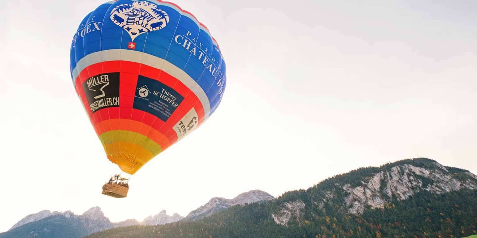 Vibrant hot air balloon flying over mountainous landscape with lush forests, promoting international school opportunities.