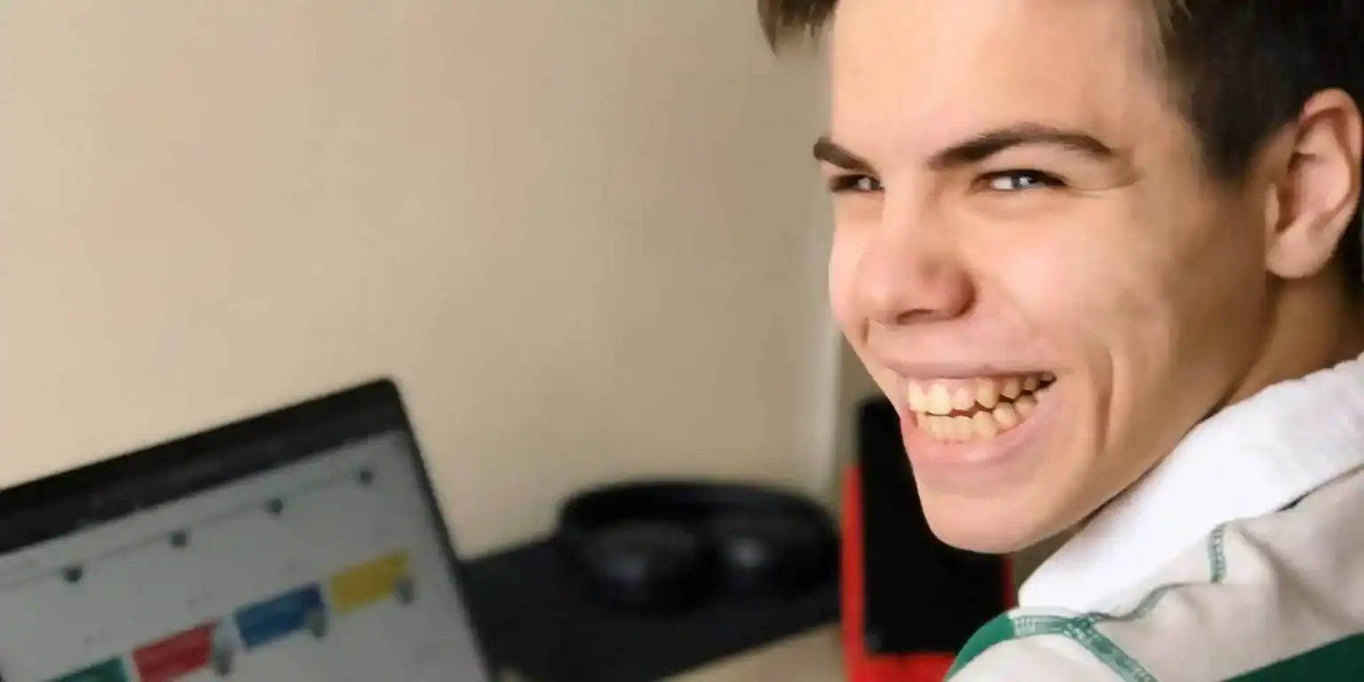Bright young student smiling at computer, studying online with focus on world schools educational programs.