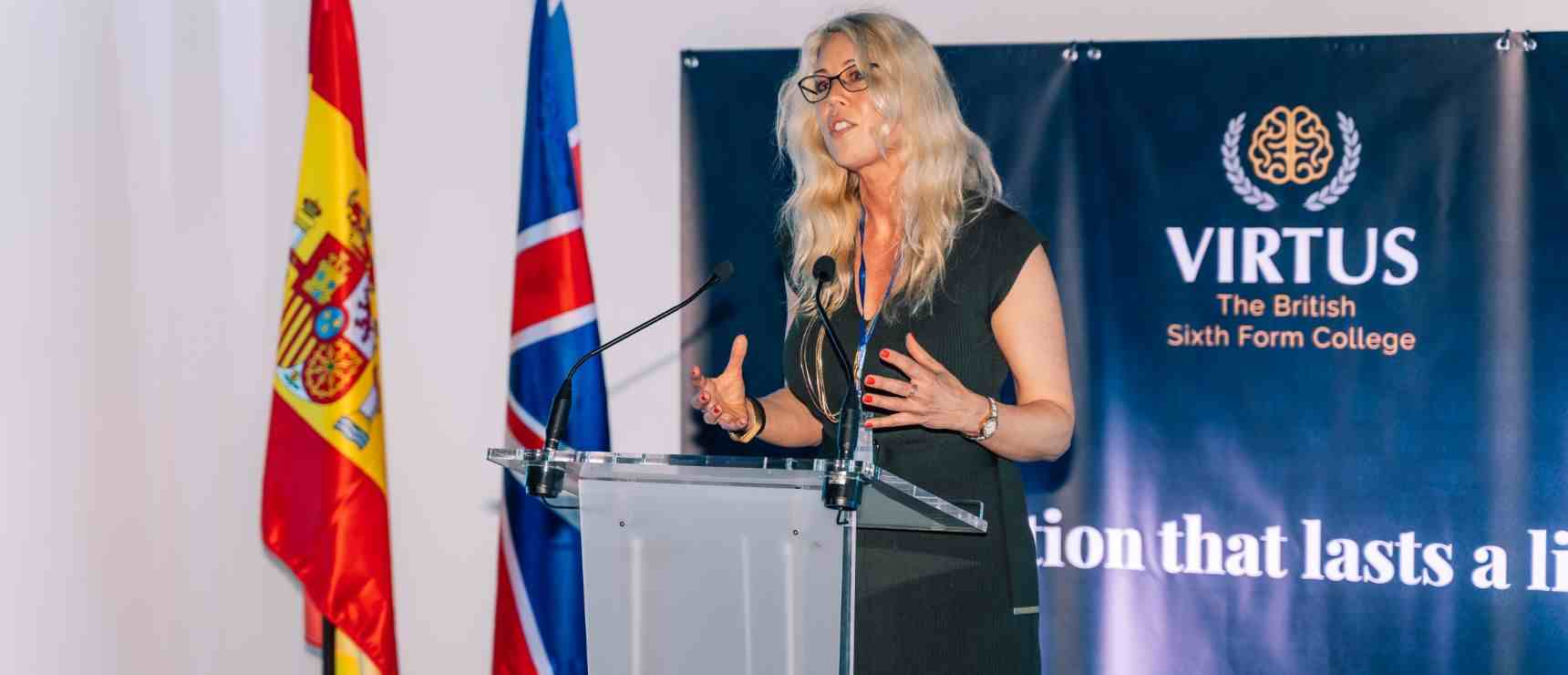 Flags of Spain and the UK with a woman speaking at a podium at Virtus British Sixth Form College.