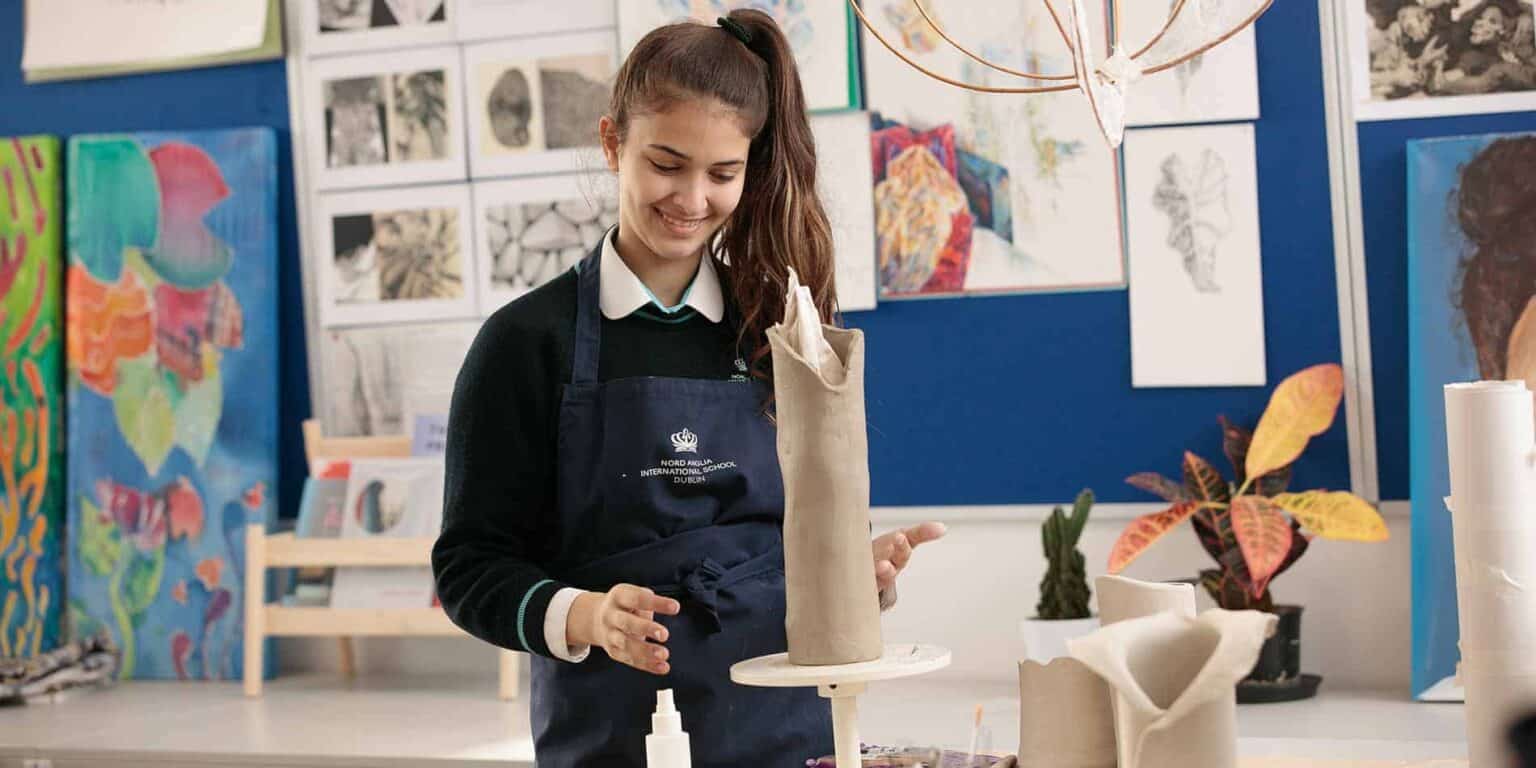 Teen girl creating pottery in art class at an international school.