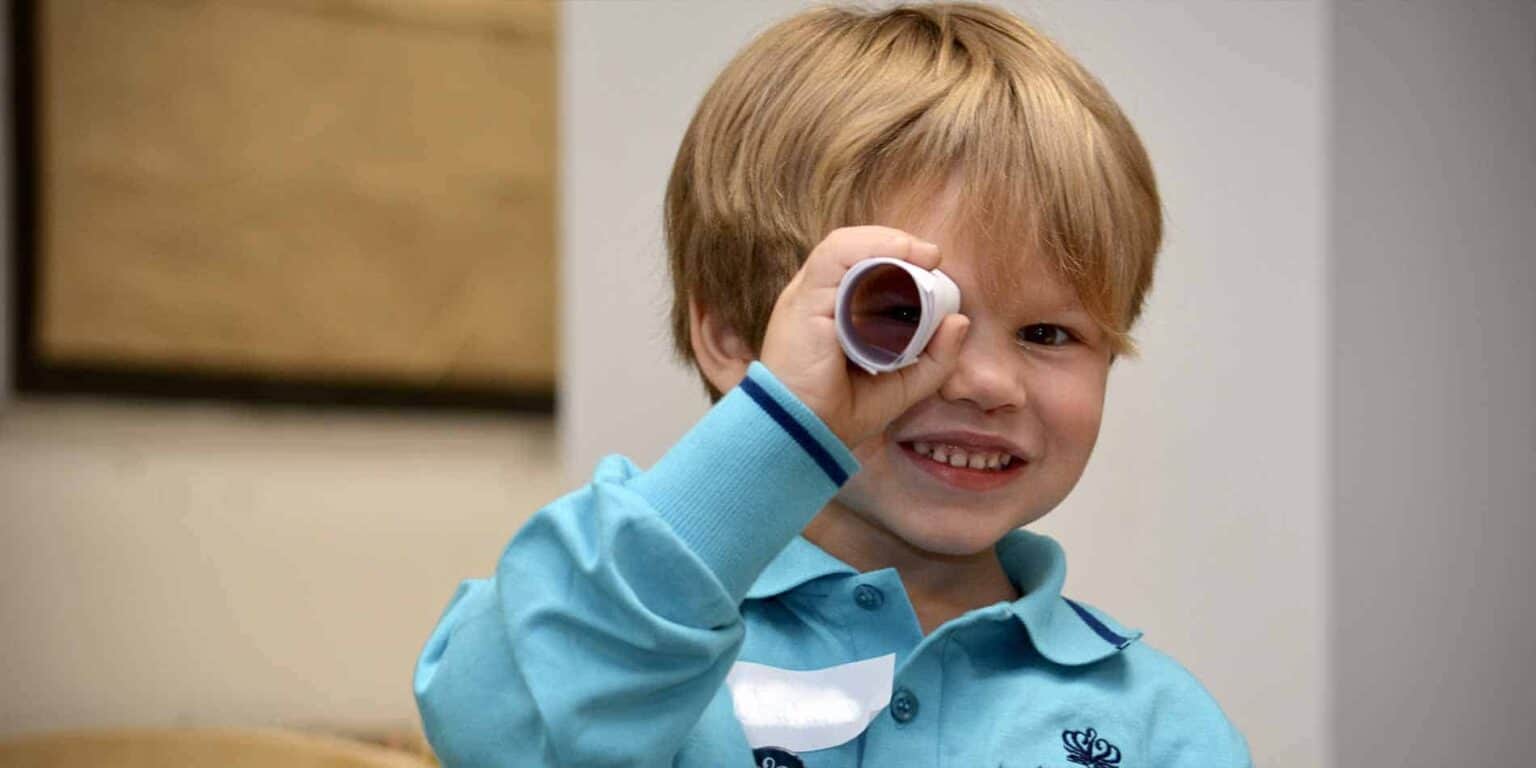 Bright young boy exploring with a toy telescope, engaging in educational activities at an international school.
