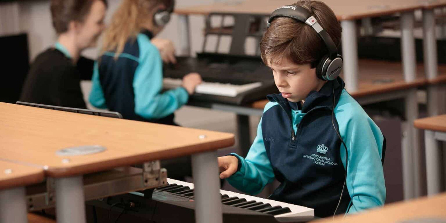 Young student wearing headphones playing piano at school music class.