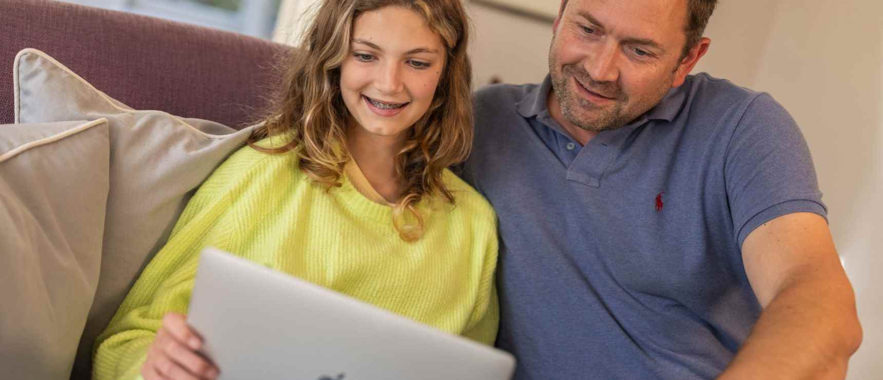 Teen girl smiling with father looking at a laptop screen at home.