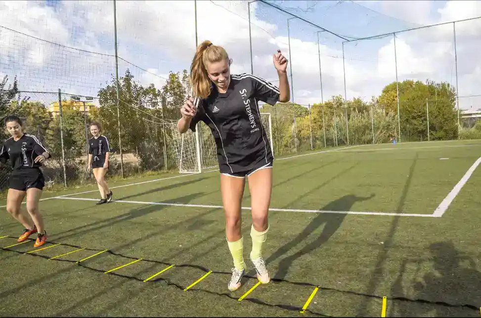 High school girls practicing agility drills on sports field, emphasizing physical education at international schools.