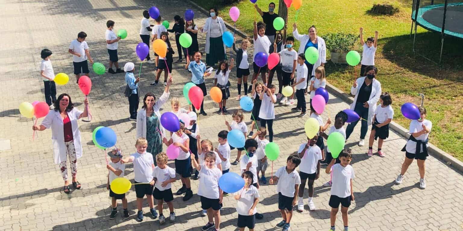 Colorful balloons with students enjoying outdoor activity at a World Schools campus.