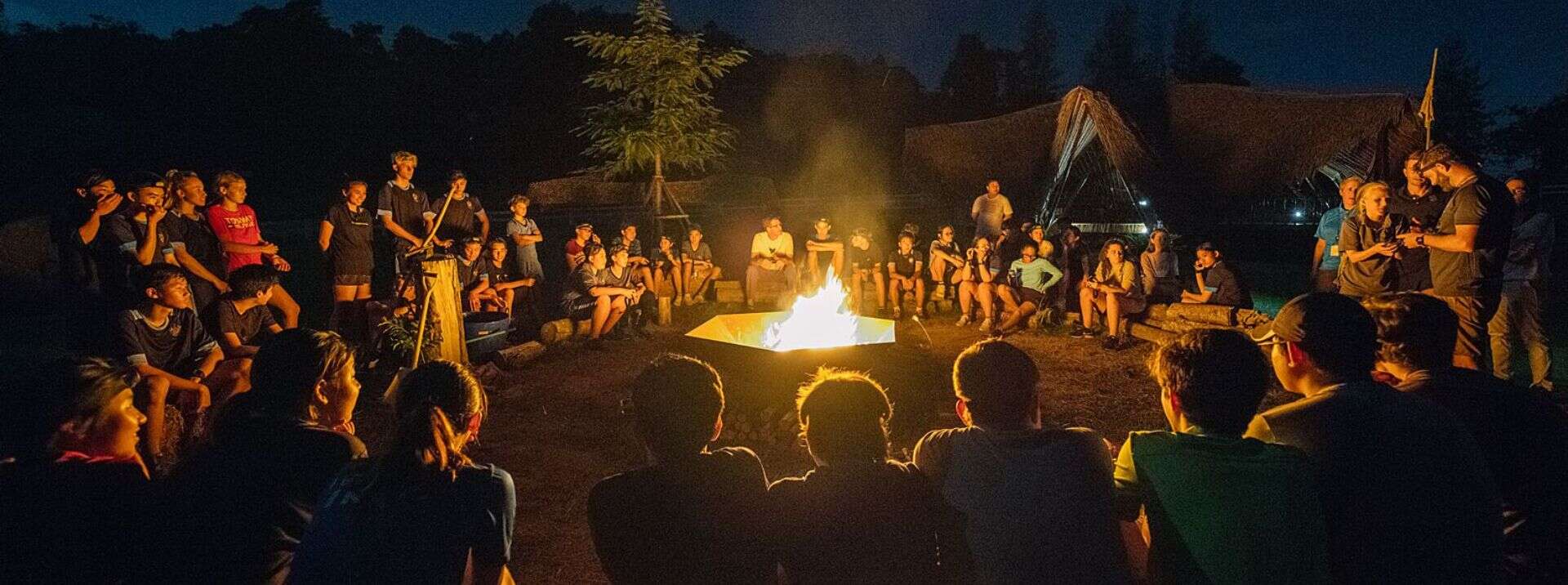 Outdoor campfire event with students sitting around at night, engaging in team-building activities.