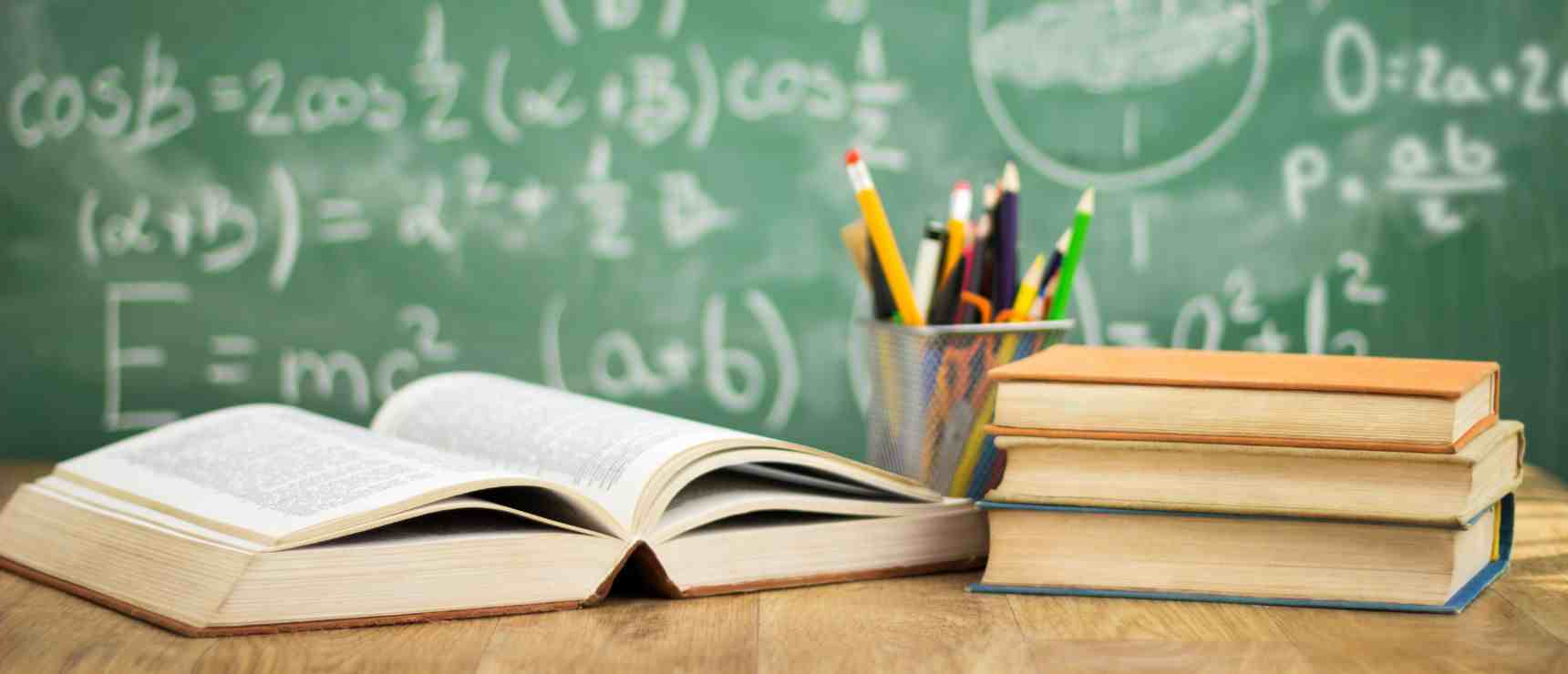 Open books and stationery in front of a chalkboard with mathematical formulas, symbolizing global school education.