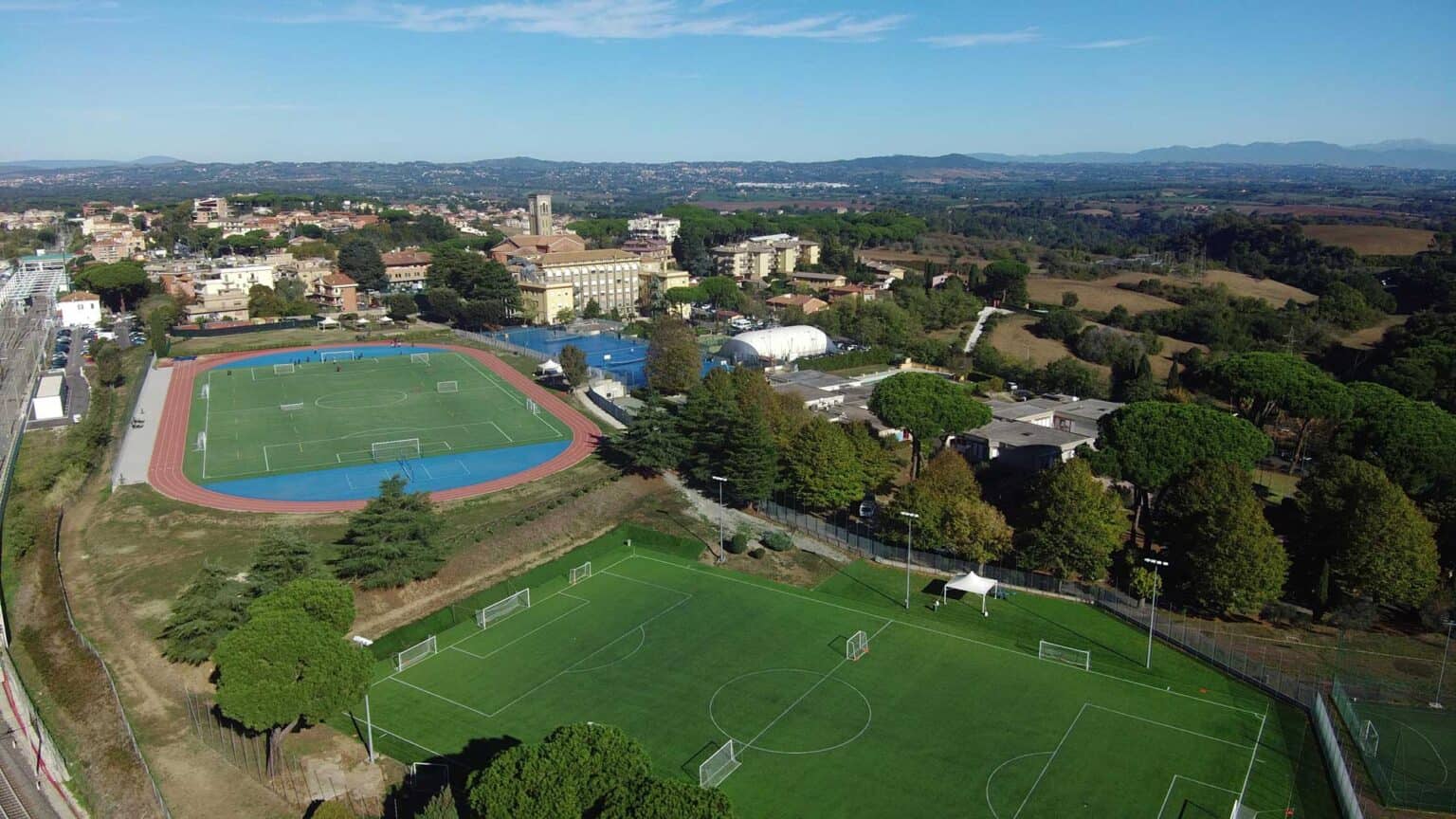 Moderni impianti sportivi scolastici internazionali con campi da calcio e piste da corsa in un campus scolastico di alta qualità.