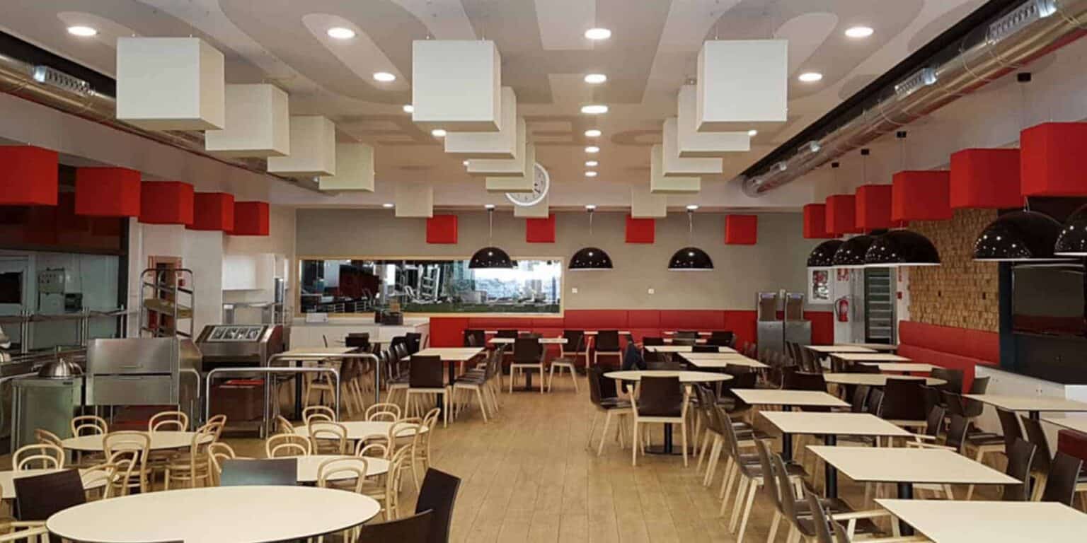 Öğrencilerin yemek yemesi için şık oturma düzenine ve çağdaş aydınlatmaya sahip aydınlık ve modern okul kafeteryası.