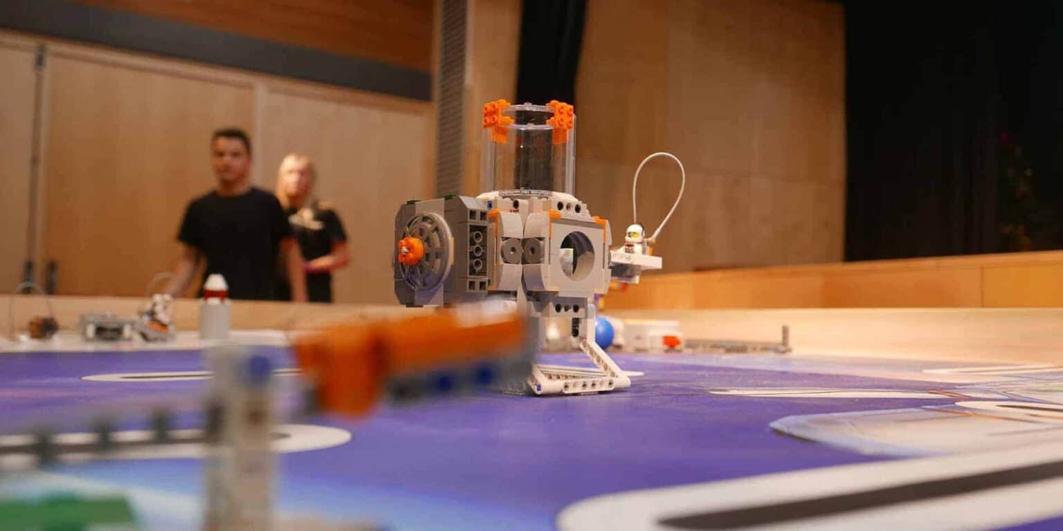 Dünya Okullarında STEM öğrenimini sergileyen, arka planda öğrencilerin bulunduğu bir okul masasındaki LEGO robotik projesi.