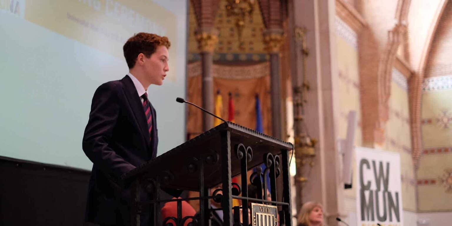 Prestijli bir uluslararası okul etkinliğinde konuşma yapan resmi kıyafetli genç bir öğrenci.