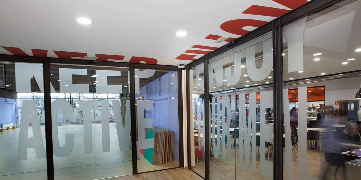 Cam kapıları ve görünür iç mekanı ile modern okul girişi, küresel öğrenciler için yenilikçi öğrenme ortamını vurgulamaktadır.