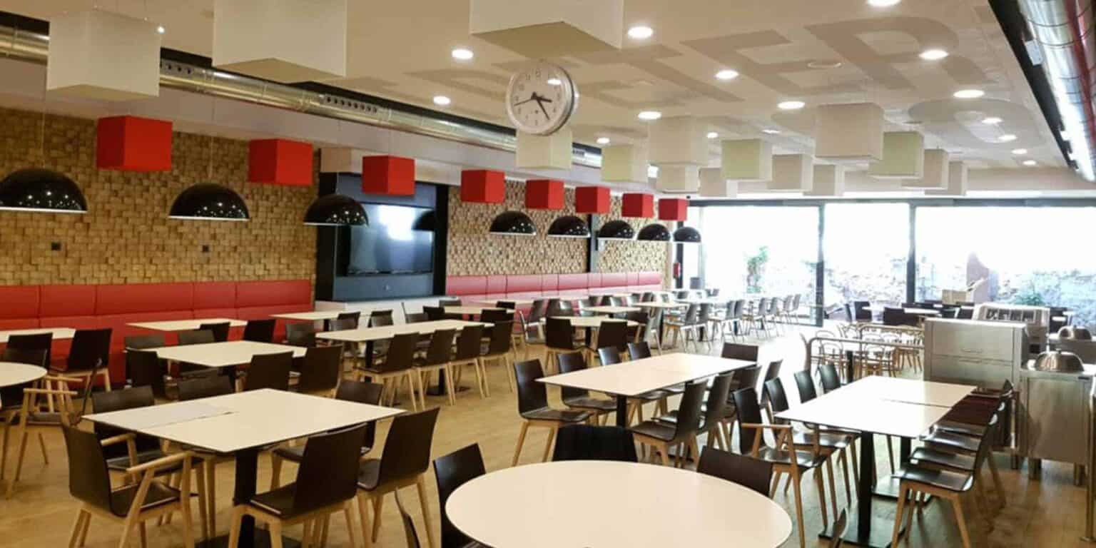 Parlak doğal ışık ve şık oturma düzenine sahip modern okul kafeteryası.