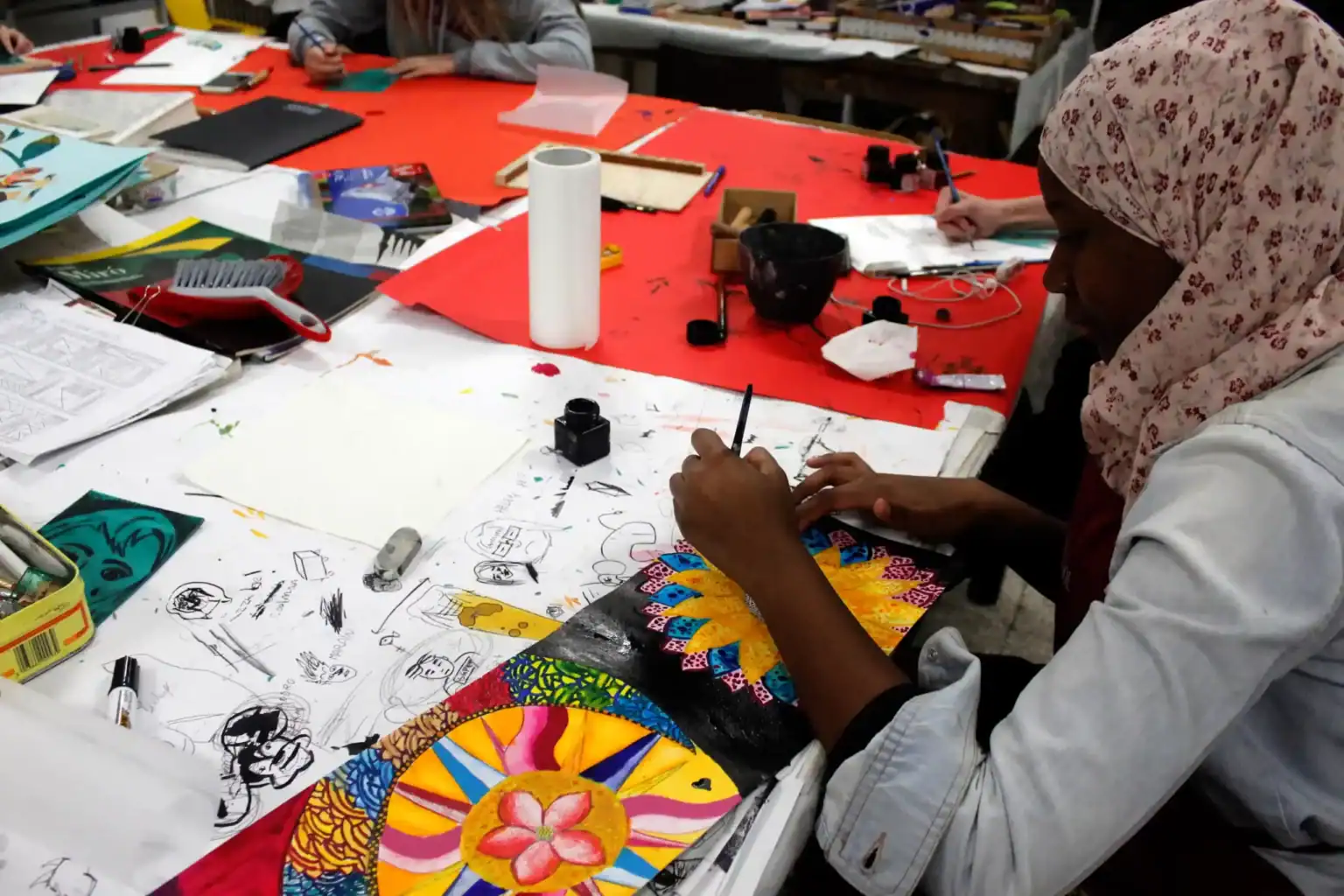 Creative student working on colorful artwork at an art classroom table.