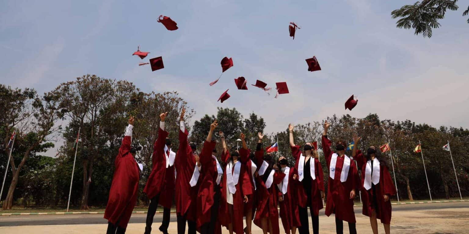 Graduates celebrating graduation ceremony outdoors with caps in air at World Schools.
