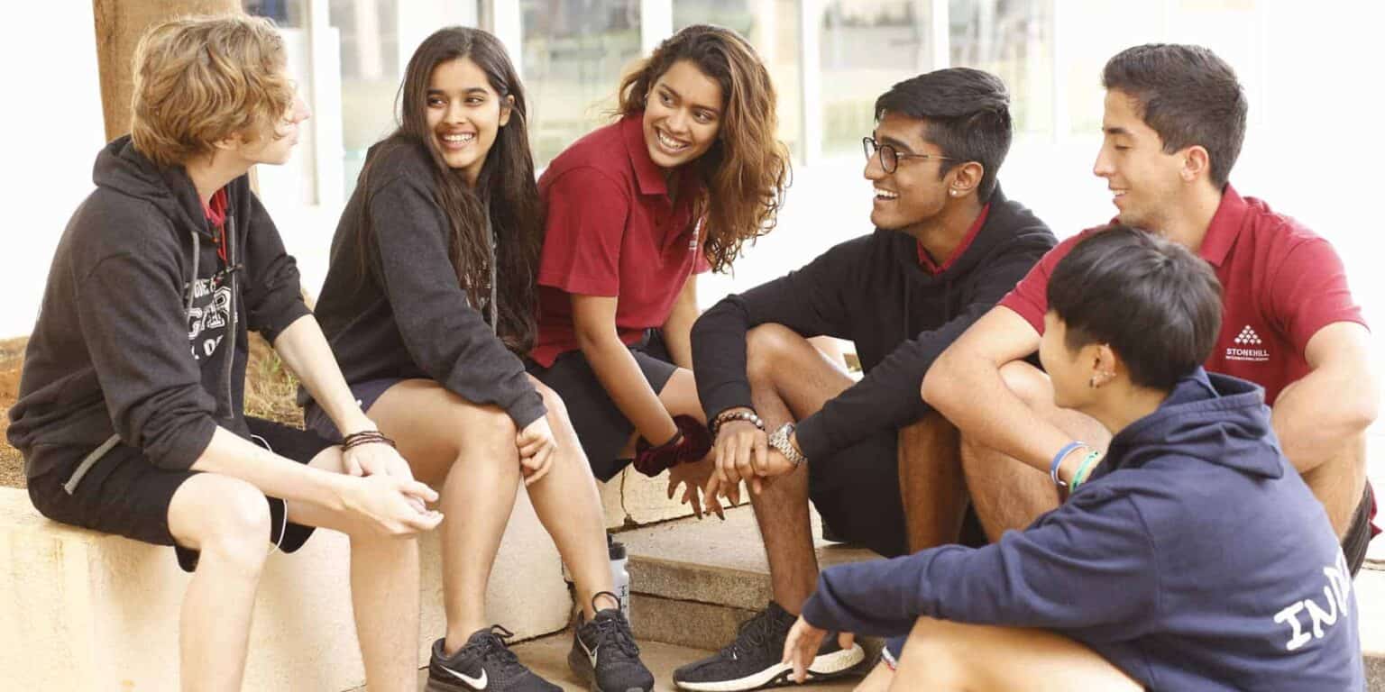 Diverse group of students chatting and laughing outdoors at World Schools campus.