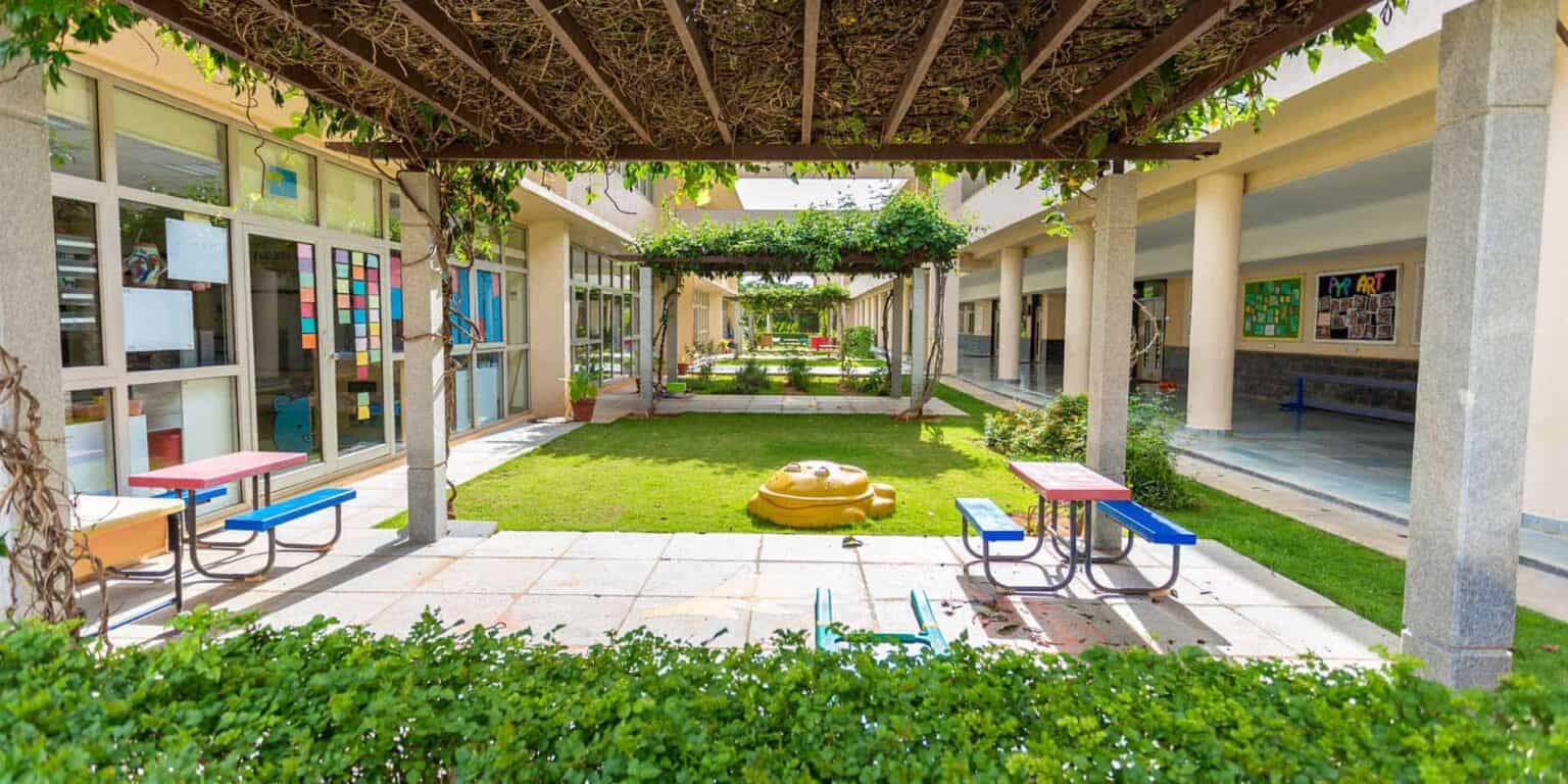 Colorful outdoor school courtyard with green grass, seating, and shaded pergolas at World Schools.