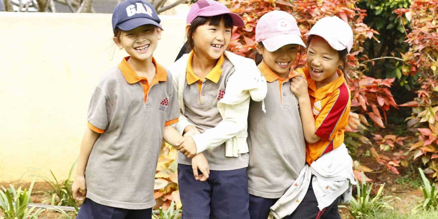 Bright young children smiling outdoors, showcasing diverse students in school uniform.