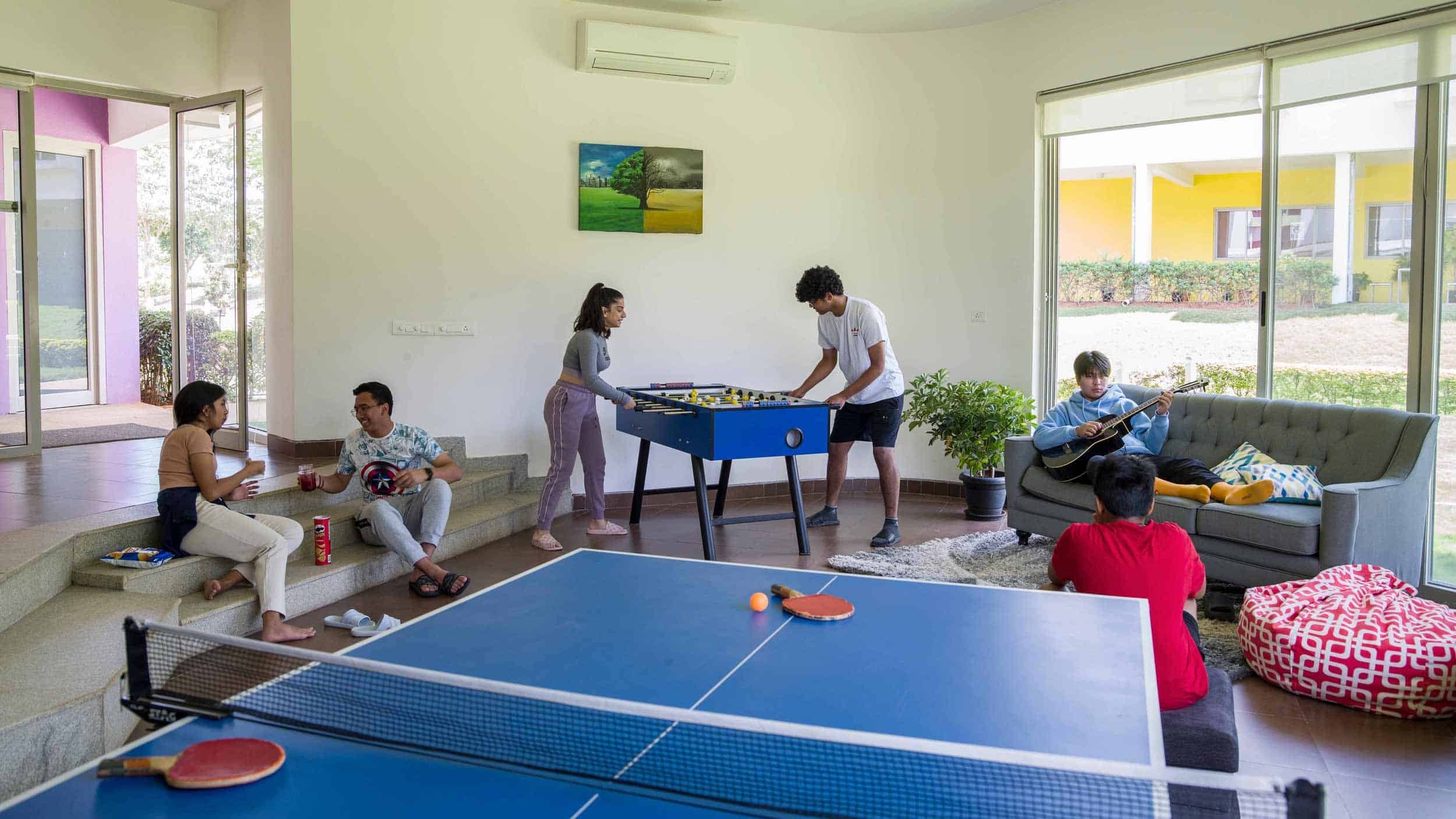 Bright modern indoor activity room with students playing foosball, doing arts, and relaxing on sofa at World Schools.