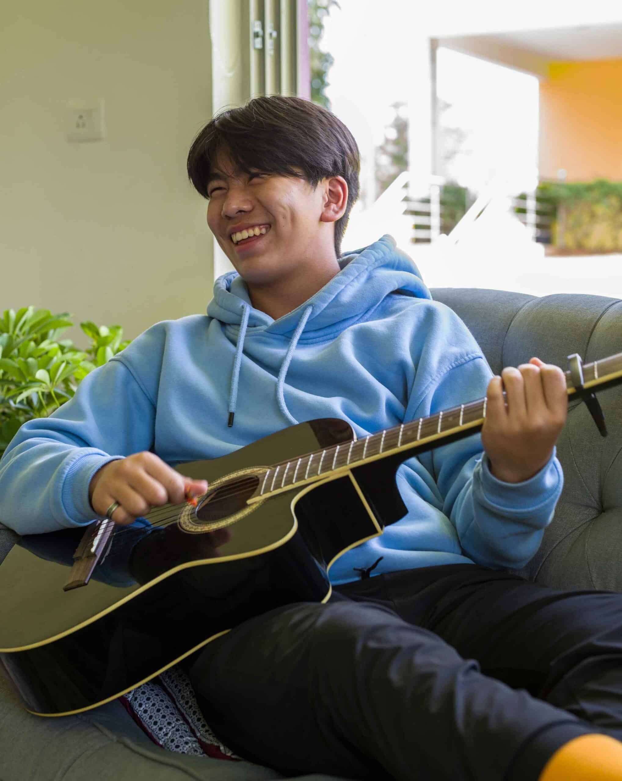 Young student playing guitar at home, enjoying music and relaxed learning environment.