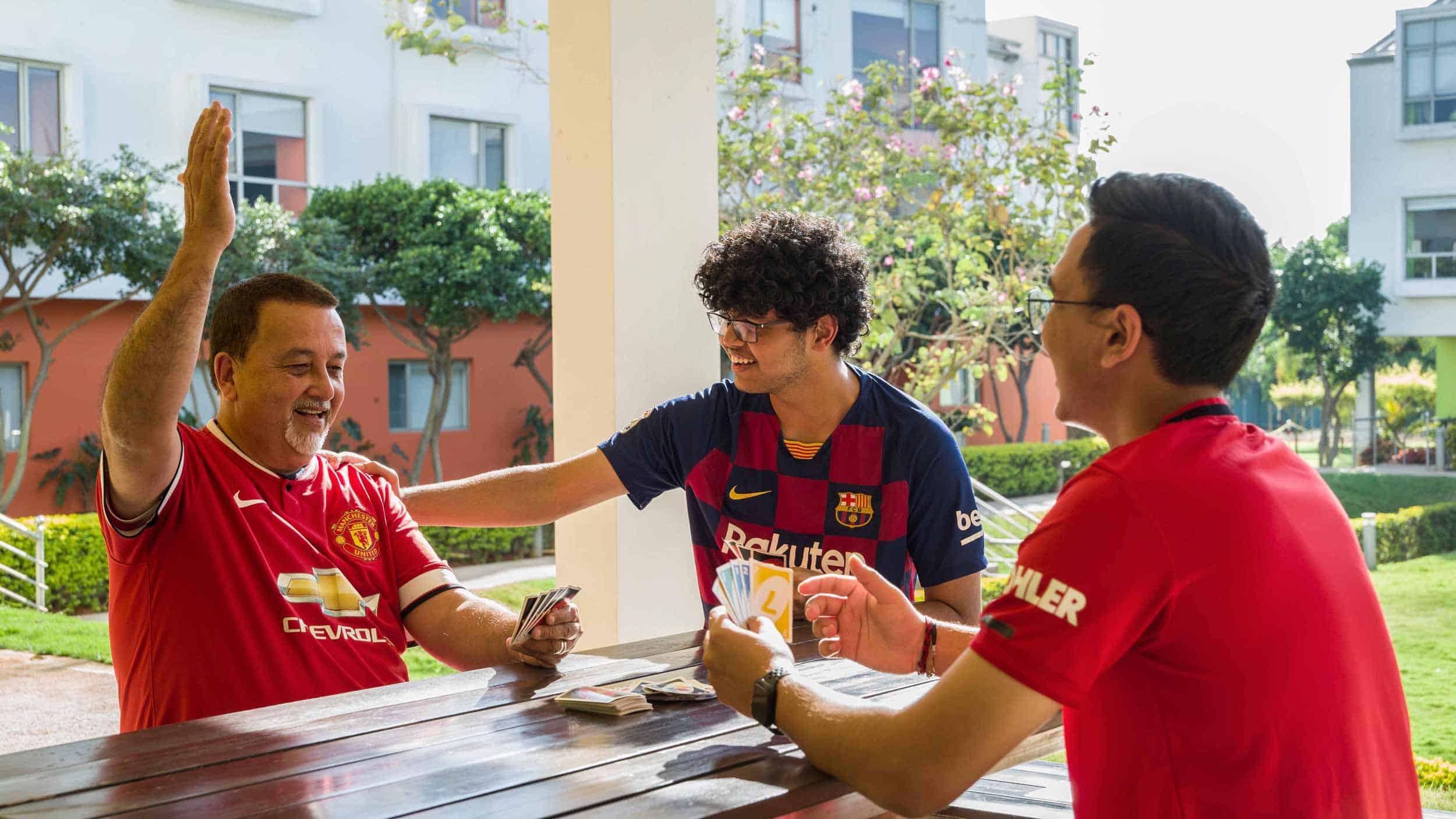 Friendly group of diverse students playing card games outdoors at a modern school campus for international learning and activities.