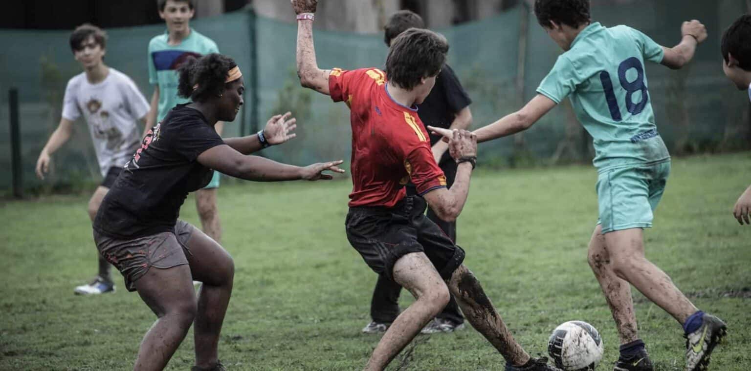 Children playing soccer on muddy field, emphasizing sports and outdoor activities at World Schools.