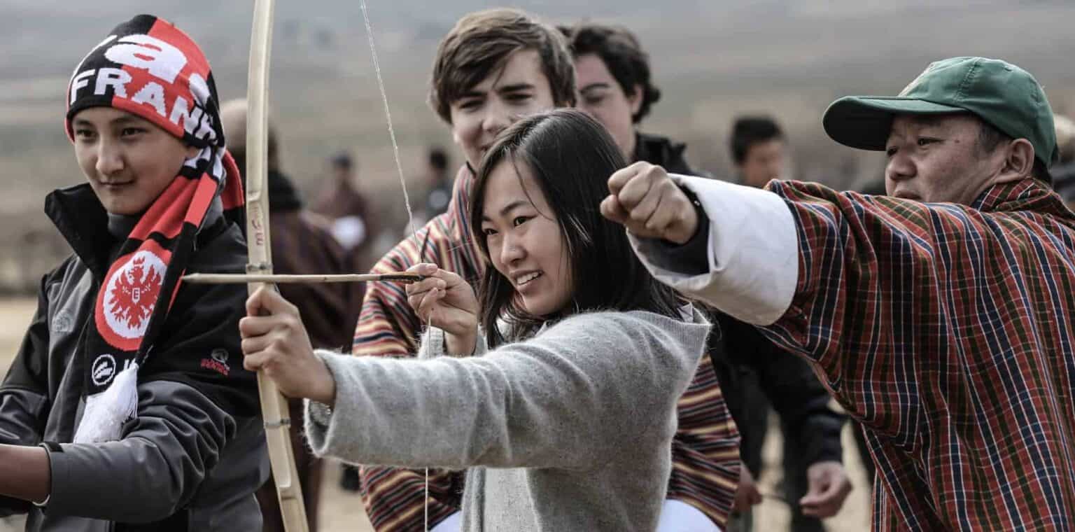 Diverse students engaging in outdoor archery activity at an international school event.