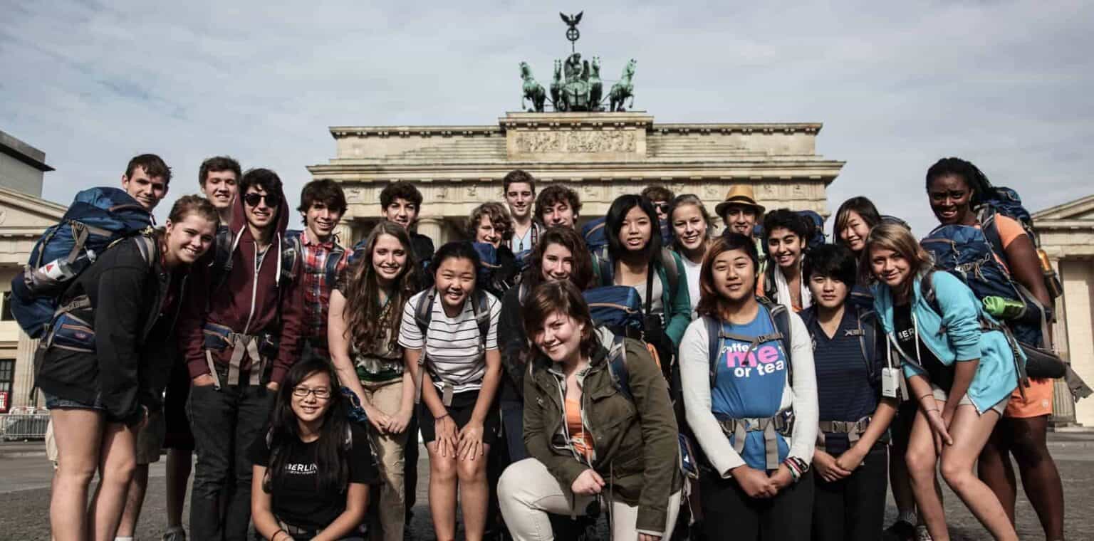 Young diverse students group sightseeing in front of Brandenburg Gate in Berlin, Germany, on educational school trip.