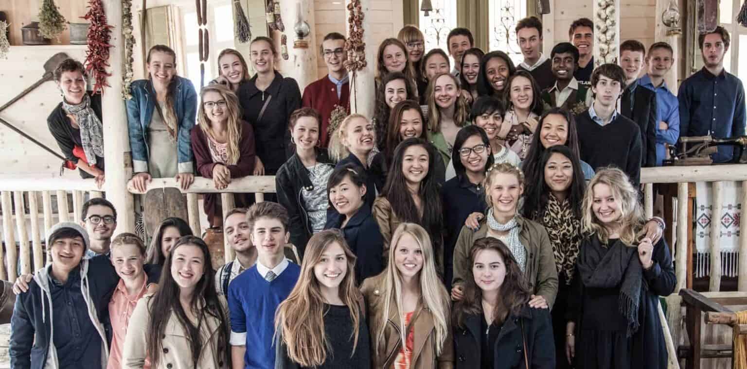 Youth school group of diverse students smiling inside a rustic wooden building with natural light.