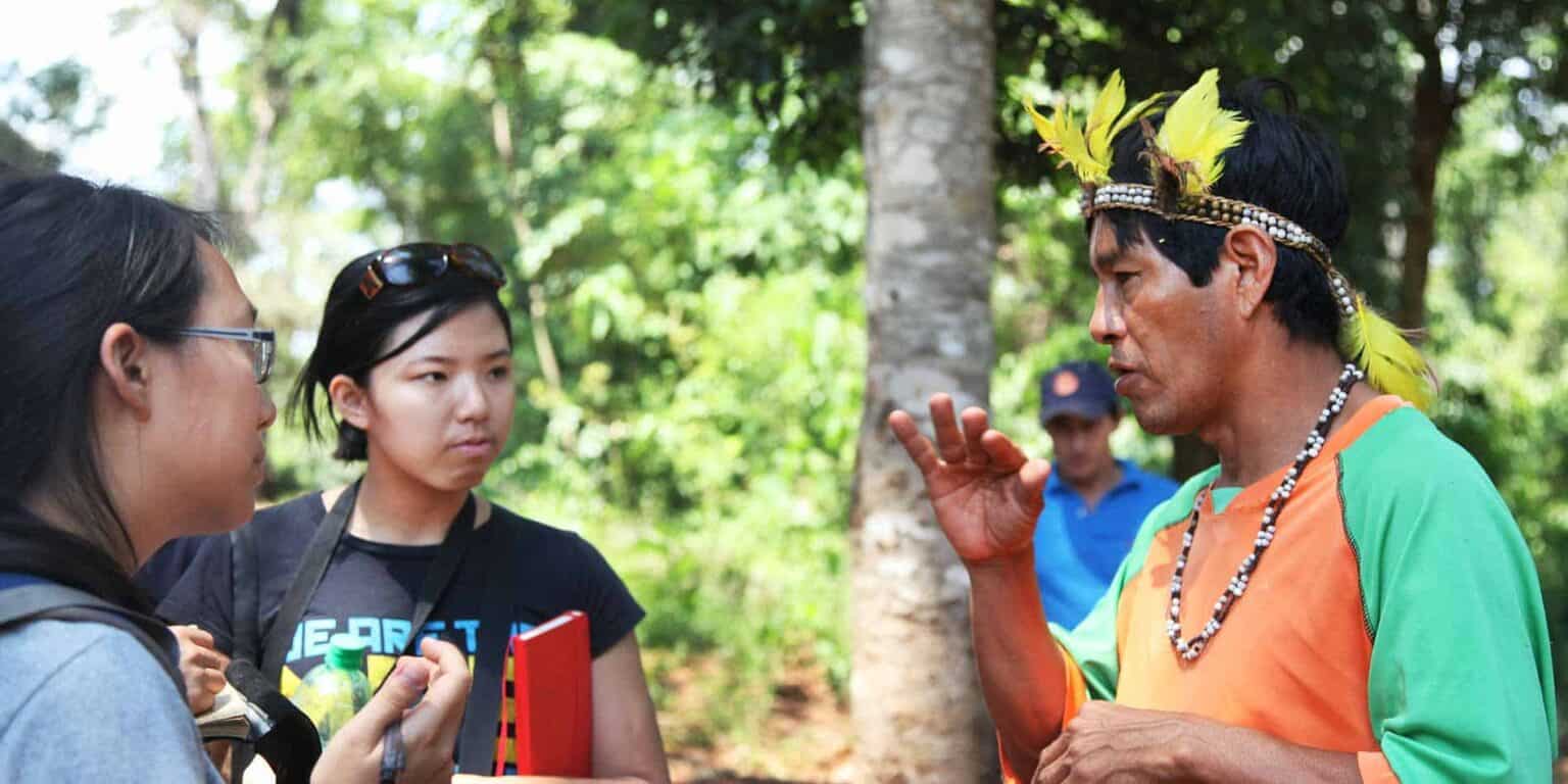 Indigenous cultural exchange with students outdoors, learning traditions in a lush forest setting.