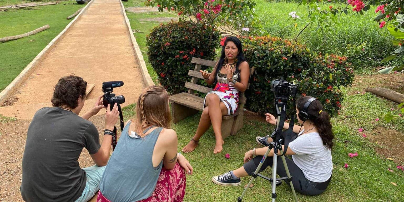 Vibrant multicultural classroom outdoor filming session with students and teacher in a lush garden setting for global education.