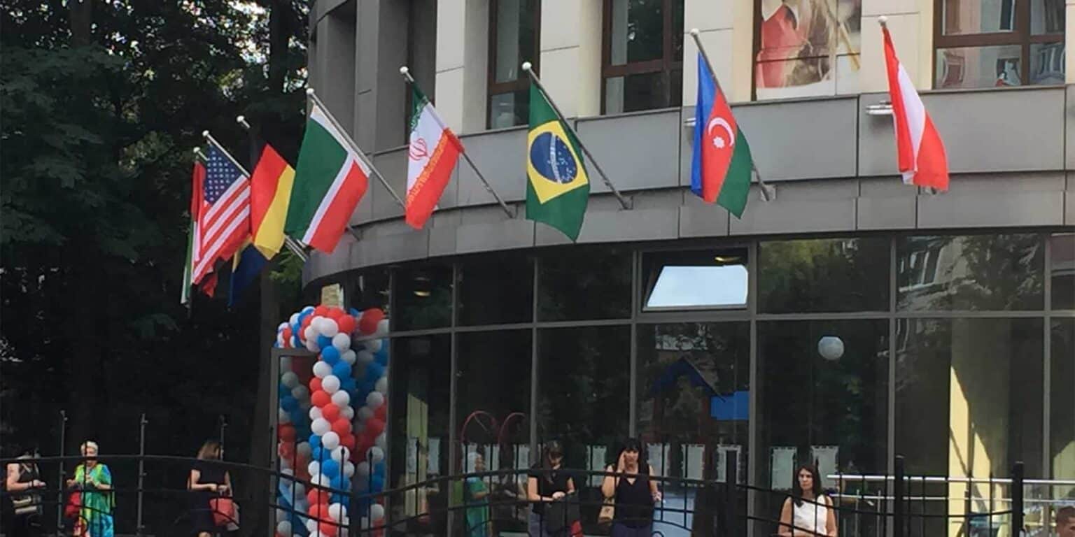 Flags of various countries flying outside a modern school building.