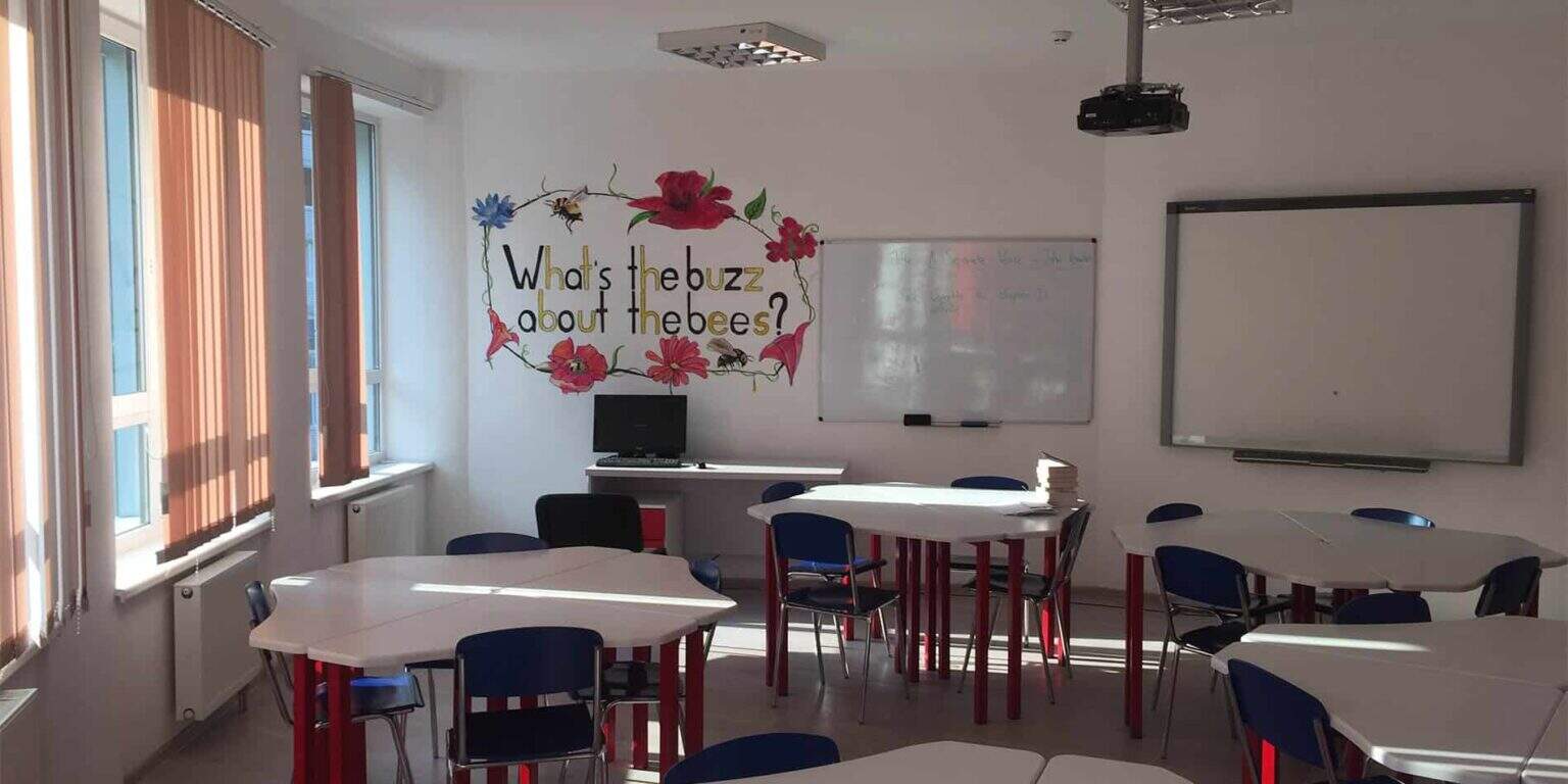 Bright classroom with whiteboards, colorful tables, and a floral "What's the buzz about the bees?" poster for engaging learning.