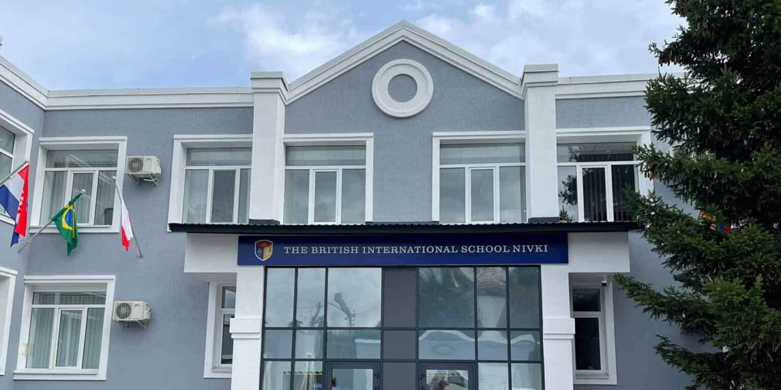 Modern British International School building with flags, glass entrance, and blue signage.