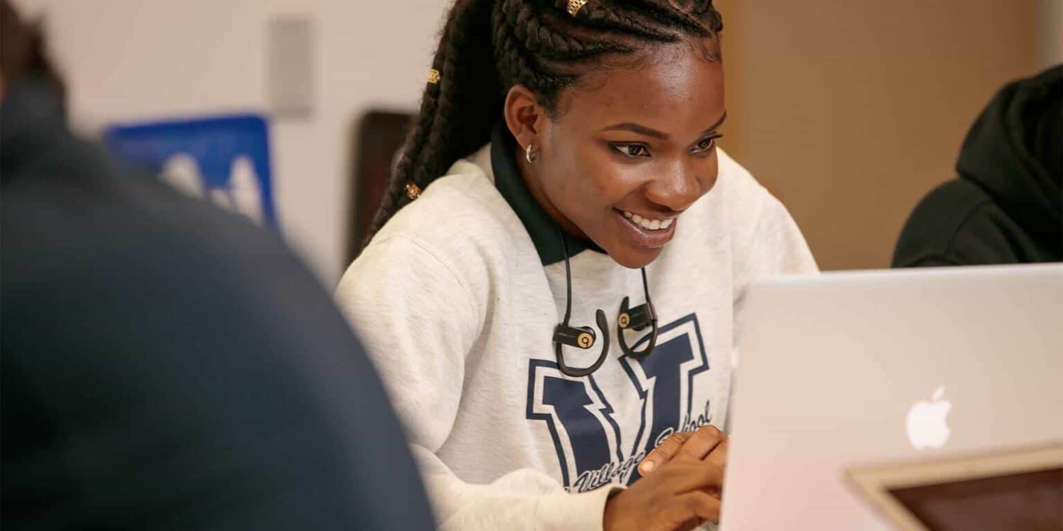 Bright African-American student smiling while working on a laptop at World Schools for quality education.